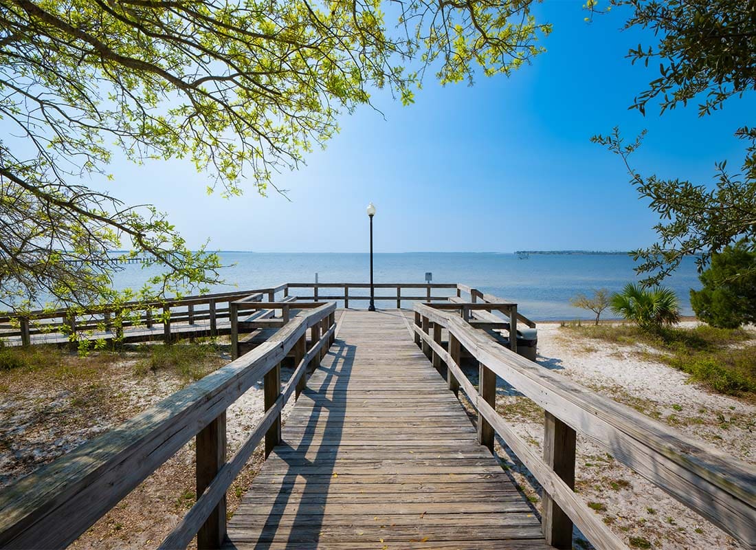 Panama City, FL - Scenic View of a Wooden Pier Surrounded by Green Foliage Leading to the Beach in Panama City Florida